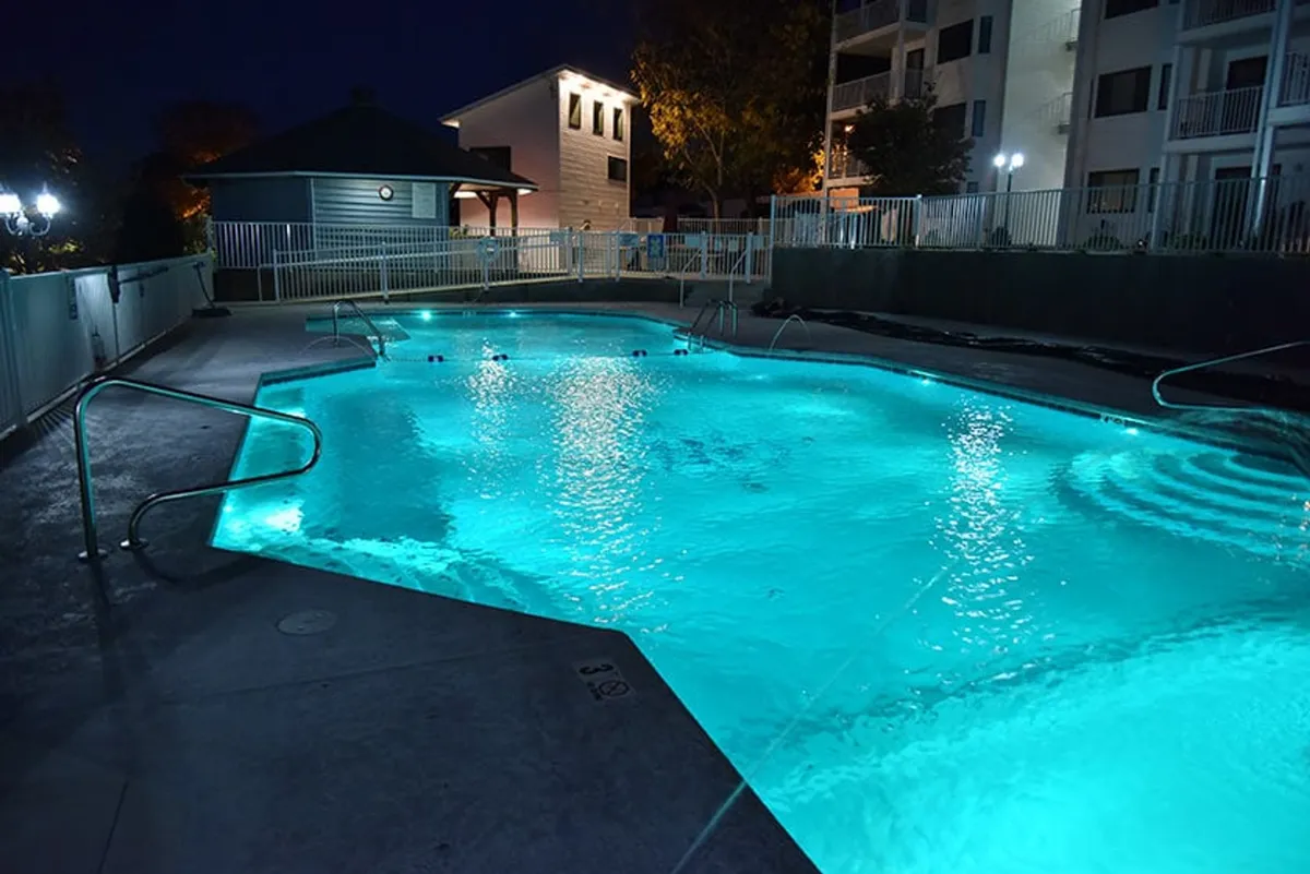 This image captures an illuminated pool surrounded by lush foliage and a deck area at night. The tranquil atmosphere hints at evening relaxation, social gatherings, and starlit swims, providing a glimpse of the leisure and community ambiance that visitors can enjoy after a day of exploring Osage Beach.