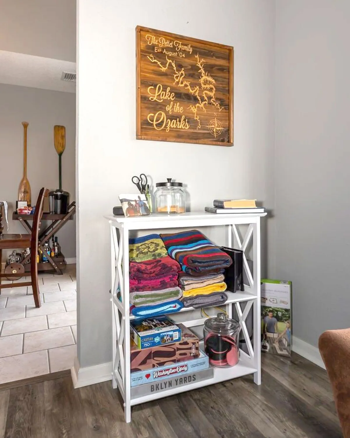 A welcoming scene featuring a wooden sign with a family name, a stack of colorful towels, a glass jar, and a collection of board games. The image radiates a sense of togetherness and fun, suggesting evenings spent bonding over games and shared experiences.
